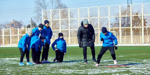 Young football player maneuvering ball through cones with focus, refining footwork during winter...