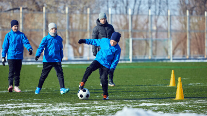 Young players practicing defensive and offensive strategies, football movements and teamwork on cold winter stadium. Discipline and performance. Concept of motivation, sport, youth, learning.