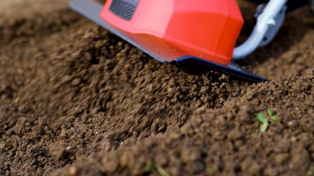 Woman preparing garden beds for planting using cultivator. Rotovator, garden tiller, rotary tiller close up. Cultivators break up compacted soil, improve its structure and aeration.