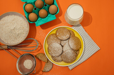 Top view of oatmeal cookies sprinkled on a yellow plate against an orange background decorated with baking materials. Cookies made from wheat flour mixed with oat cereal, a traditional pastry