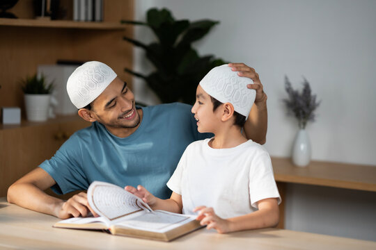 Muslim father and son in mosque praying and reading holly book Quran together. Happy learning Islamic education concept. A man pround with hiis boy, looking each other and smile.