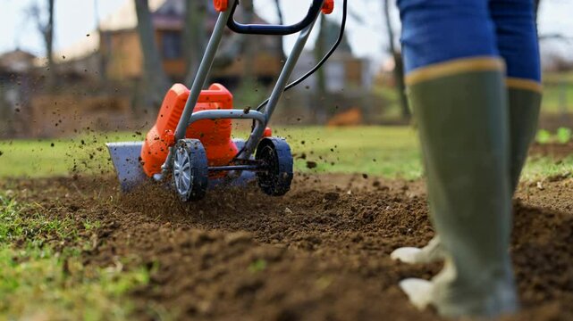 Woman preparing garden beds for planting. Rotovator, garden tiller, rotary tiller or mini cultivator. Cultivators break up compacted soil, improve its structure and aeration.