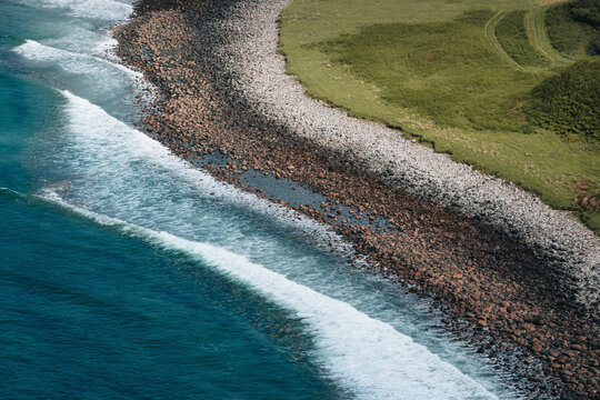 Aerial view of beautiful coastline with waves crashing on rocky shore and grassy terrain, Highlands, Scotland, United Kingdom.
