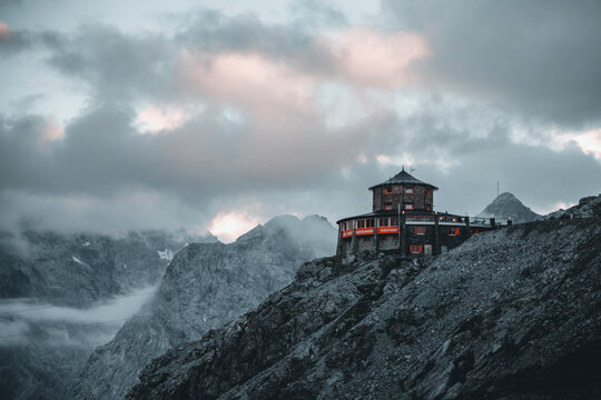 Stelvio, Italy - 29 June 2022: Aerial view of majestic dolomites with a serene cabin amidst rocky peaks and cloudy sky, Stelvio, Italy.