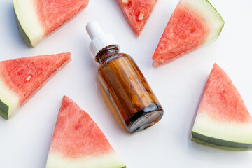 A sleek black frosted serum bottle elegantly placed beside fresh watermelon slices on a soft...