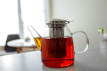 Freshly brewed tea in a glass kettle on a kitchen countertop at midday