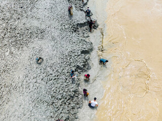 Feni, Bangladesh - 27 August 2024: Aerial view of people fishing with handmade nets in flood water along the muddy Feni riverbank, Feni, Chittagong, Bangladesh.