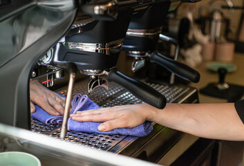 Unrecognizable barista cleaning espresso machine with purple cloth in coffee shop