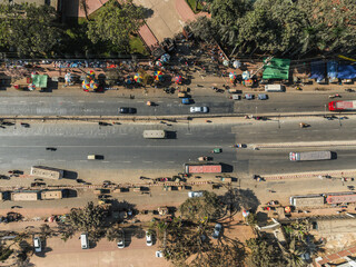 Aerial view of busy urban road with cars and market stalls surrounded by greenery, Pathalia, Savar, Dhaka, Bangladesh.