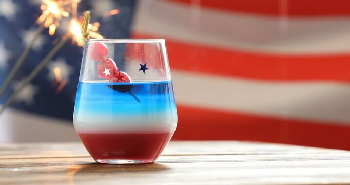 Woman adding maraschino cherries to cocktail at wooden table against American flag, closeup. Space for text