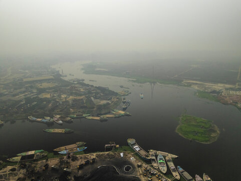 Aerial view of buriganga river with boats and docks amidst a foggy urban landscape, Amin Bazar, Savar, Dhaka, Bangladesh.