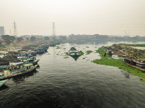 Aerial view of a serene river with boats and calm water surrounded by greenery and buildings, Amin Bazar, Savar, Dhaka, Bangladesh.