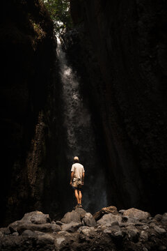 Tourist admiring majestic waterfall in rocky gorge during mount meru trekking, tanzania. Tourist observing stunning waterfall in a dark gorge during mount meru trekking in tanzania, africa