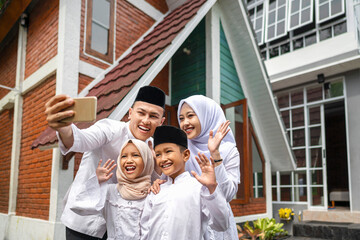 Indonesian Muslim family with a mobile phone taking a selfie or video call while celebrating Eid Mubarak. Concept of Happy Lebaran, Eid Al Fitr, Idul Fitri, and Ramadan Mubarak celebration © Leo Lintang