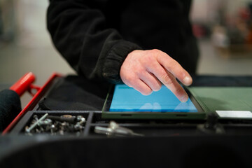 Industrial mechanic professional in modern digitalized workshop garage business operating smart tablet device with touchscreen ordering different spare parts in website for e-commerce
