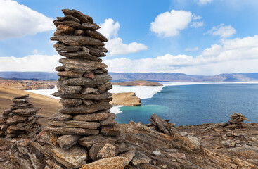 Spring landscape of Baikal Lake with a traditional stone pyramid on a high cape. View of the Small Sea and Olkhon Gate Strait during ice drift on sunny April day. Spring travels and outdoor recreation