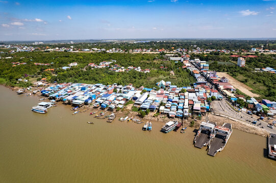 Aerial view of a scenic riverside town with houses, boats, and docks under a blue sky, Akreiy Ksatr, Kandal, Cambodia.