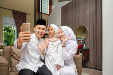 Portrait of the Indonesian Muslim family with mobile phone taking selfie or video call while...