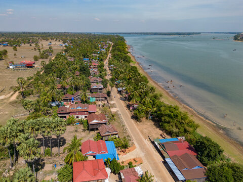 Aerial view of a picturesque village with houses and a serene river surrounded by lush greenery and palm trees, Thala Barivat District, Stung Treng, Cambodia.