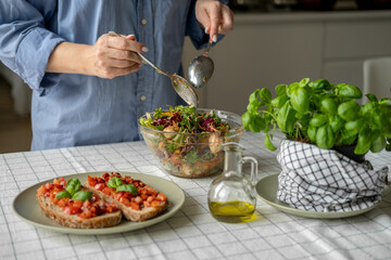 Women's hands mix salad with tomato tomato mozzarella vegetables and arugula in a large bowl for an easy diet lunch or dinner, a healthy balanced meal	