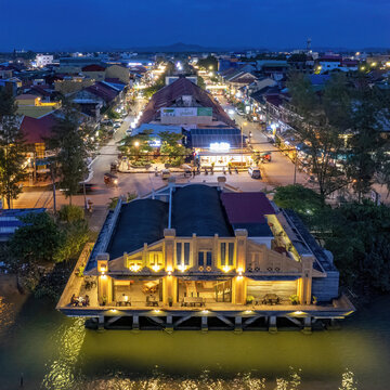 Tuek Chhou District, Cambodia - 18 September 2022: Aerial view of vibrant cityscape with illuminated buildings and serene waterfront reflections at dusk, Kampong Kandal, Kampot, Cambodia.