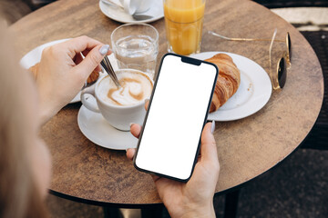 Mockup woman's hand holding using smart phone with white blank screen POV at coffee shop, mobile...