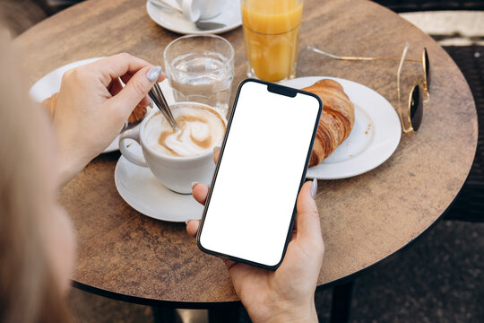 Mockup woman's hand holding using smart phone with white blank screen POV at coffee shop, mobile app design and advertising, online marketing