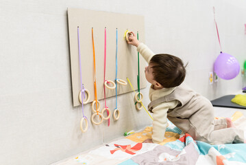 Baby boy playing with colorful ribbon and wooden rings on sensory board, developing fine motor skills