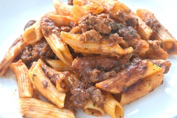 baking penne pasta topping mashed beef meat in sweet and sour sauce on plate    
