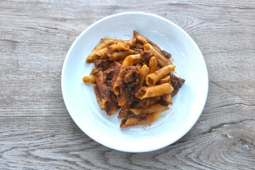 baking penne pasta topping mashed beef meat in sweet and sour sauce on plate    