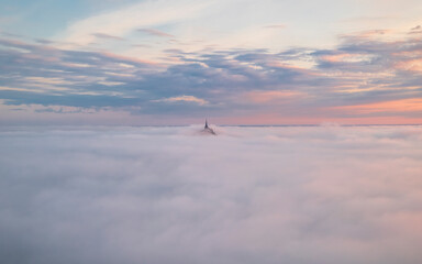 Aerial view of the majestic Mont Saint-Michel surrounded by soft clouds and a picturesque sky at sunset, Le Mont-Saint-Michel, Manche, France.