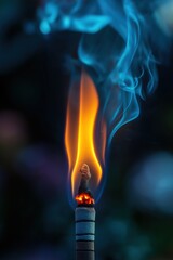 Burning incense stick with blue smoke and orange flame on dark background