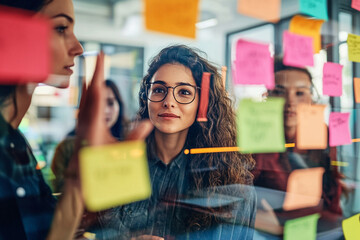 Professional Diverse business team engaging in innovative brainstorming session with colorful sticky notes on glass wall. Creative professionals sharing, discussing, and visualizing ideas using des...