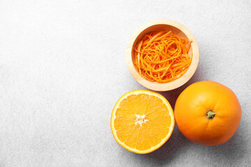 Fresh orange zest in bowl, whole and cut fruits on grey textured table, flat lay. Space for text