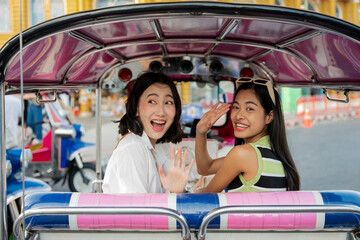 Two happy tourists waving from a tuk tuk in Bangkok