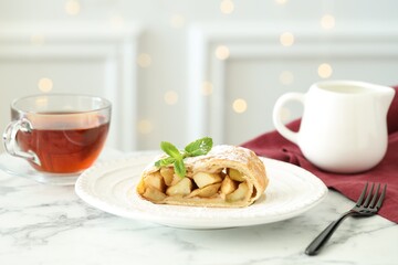 Piece of tasty apple strudel served with tea on white marble table, closeup