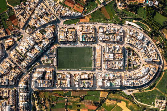 Aerial view of a vibrant football field surrounded by residential buildings and streets in Dingli, Malta.