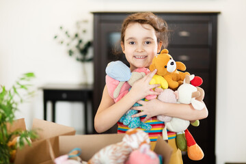 Happy cute little kid girl having fun after moving into a new home. Child with cardboard boxes with...