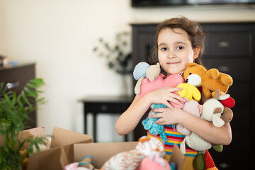 Happy cute little kid girl having fun after moving into a new home. Child with cardboard boxes with...