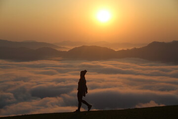 Obraz premium silhueta de mulher em topo de montanha com mar de nuvens e sol nascendo no horizonte - foto tirada no morro são bernardo em rio dos cedros, santa catarina 