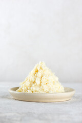 Heap of shea butter in a plate on a light background. Vertical orientation.