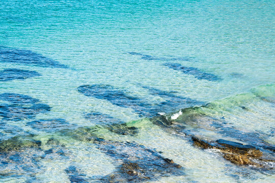 Crystal clear, blue sea water rippling over rocks and white sand