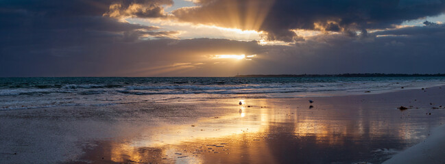 Golden sunshine breaking through dark clouds at sunset over a beach