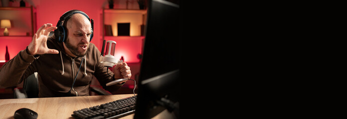 Gamer streamer playing online game on PC in dark room. Emotional and aggressive shouting in...