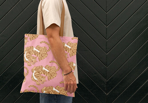 Mockup of a Man Holding a Tote Bag Against a Dark Textured Wall