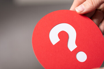 Hand holding a red circle with a white question mark.  Uncertainty concept.