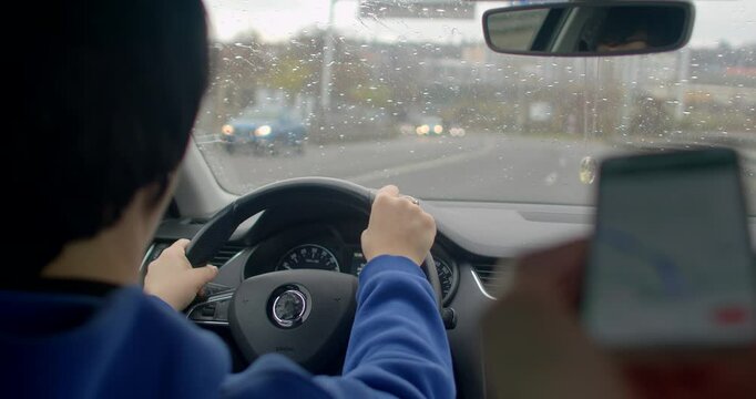 A driver is using their smartphone to access navigation features while driving on a rainy road