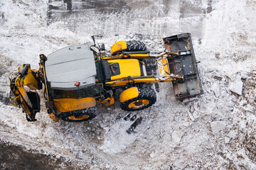 Yellow tractor clearing snow on winter road, aerial top view. Consequences of natural disaster...