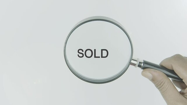Sold text or word highlighted by a magnifying glass in a hand on a white background, symbolizing focus on transactions, completion, and finalizing deals
