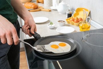 Man taking fried eggs from frying pan in kitchen, closeup